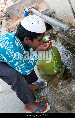 Garçon musulman indien l'eau potable à partir d'un robinet à l'extérieur d'une maison à Bukkapatnam, Andhra Pradesh, Inde Banque D'Images