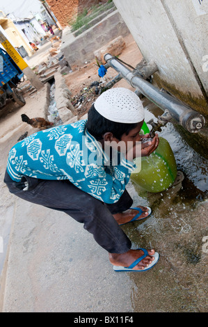 Garçon musulman indien l'eau potable à partir d'un robinet à l'extérieur d'une maison à Bukkapatnam, Andhra Pradesh, Inde Banque D'Images