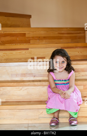 Happy little girl en robe rose assis sur l'escalier à la maison Banque D'Images