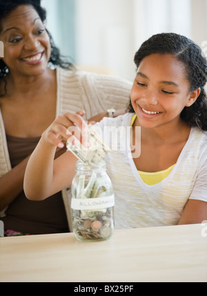 Mère regardant fille mettre de l'argent dans jar Banque D'Images
