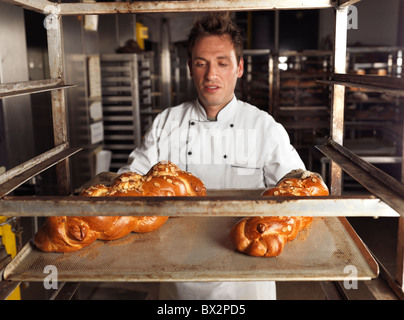 Baker en tenant un plateau avec du pain tressé challah douce hors d'un rack trolley dans une boulangerie. L'accent est mis sur le pain Banque D'Images