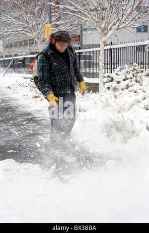 L'homme à l'aide de la souffleuse à neige pour dégager la neige et la glace d'un sentier public Banque D'Images