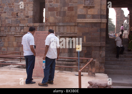 Les touristes de la lecture d'un signe à l'intérieur du complexe Qûtb Minâr à New Delhi, en Inde. Signe de visite audio avec des marches en arrière-plan Banque D'Images