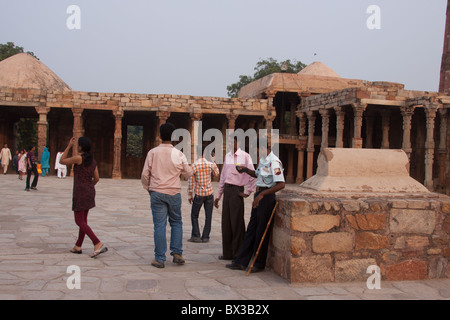 Les touristes, debout près de la colonne de fer à côté du Qutub Minar à New Delhi, en Inde avec un garde de sécurité appuyé contre le tombeau. Banque D'Images