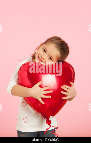 Une jeune fille tenant un ballon en forme de coeur rouge Banque D'Images