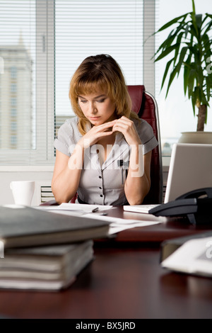 Photo de belle femme assise au milieu de travail dans le bureau et la lecture de document Banque D'Images