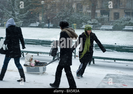 Femme à l'aide d'un panier de lavage comme un traîneau pour tirer son enfant dans la neige dans un parc de Paris. Banque D'Images