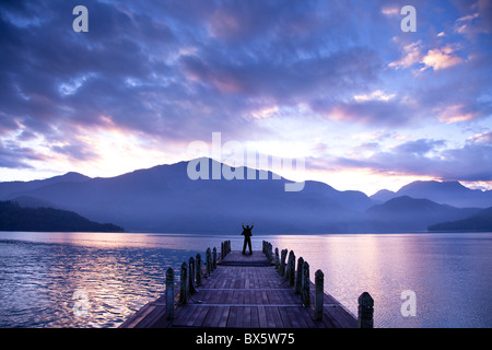 Homme debout sur un quai et regarder les montagnes et le lac Banque D'Images