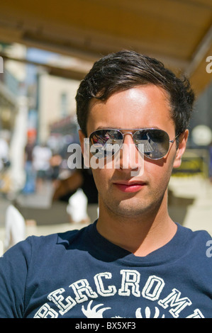 Jeune homme portant des lunettes de soleil Ray Ban assis dans Sun Banque D'Images