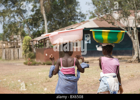 Les filles avec des seaux en équilibre sur leurs têtes à pied le long de la rue principale de Kakata, au Libéria, en Afrique de l'Ouest. Banque D'Images