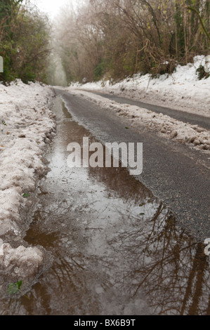 Poule et la fonte des neiges de l'écoulement dans une route de campagne causés par la neige et le temps de gel Banque D'Images