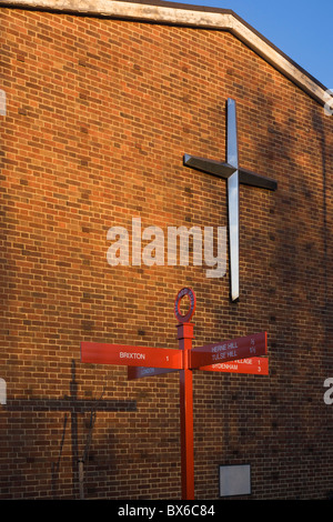 La croix sur le mur de Herne Hill's United Reform Church et la direction sign post (et son ombre) de Red poster Hill. Banque D'Images