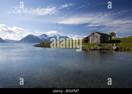 Cabine avec toit d'herbe traditionnelle surplombant un fjord et montagnes enneigées Lyngen en Péninsule, comté de Troms, Norvège Banque D'Images