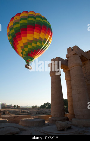 Une belle et colorée hot air balloon flotte doucement sur les statues et les ruines d'un ancien temple égyptien au lever du soleil Banque D'Images