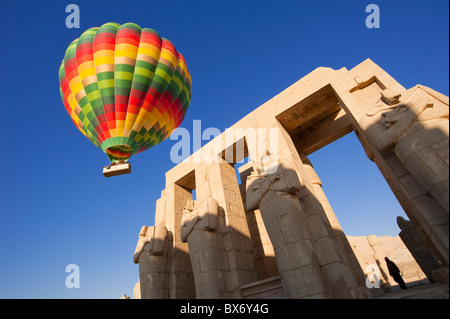 Une belle et colorée hot air balloon flotte doucement sur les statues et les ruines d'un ancien temple égyptien au lever du soleil Banque D'Images