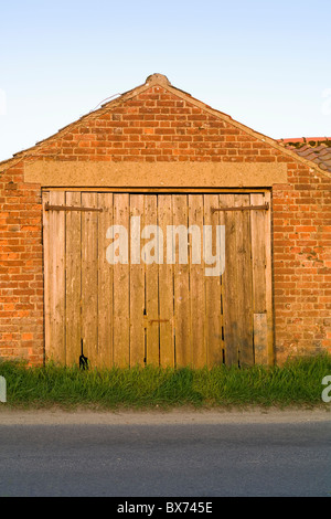 Ancienne grange en brique rouge avec porte en bois face à Road Banque D'Images