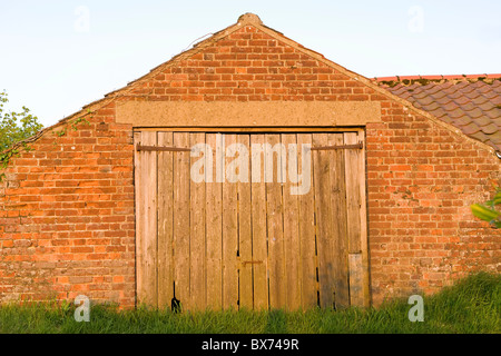 Ancienne grange en brique rouge avec porte en bois face à Road Banque D'Images