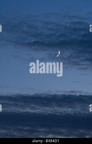 Un croissant de lune brille derrière banderolles de nuages au-dessus de la péninsule de Lleyn au coucher du soleil. Banque D'Images