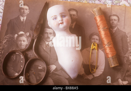 Reptile dépourvu de corps et tête de poupée en porcelaine classique couché avec des ciseaux la goupille de sécurité et bobine de fils à coudre sur la vieille photo de famille Banque D'Images