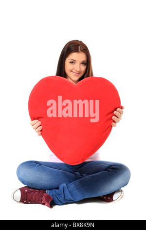 Attractive young woman holding oreiller rouge en forme de cœur. Le tout sur fond blanc. Banque D'Images