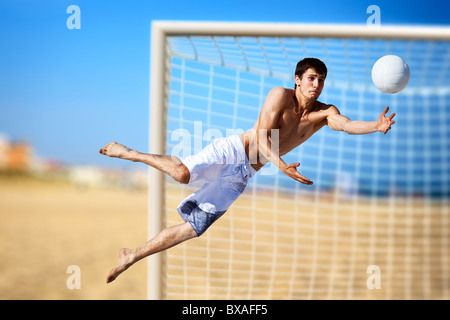 Jeune homme jouant au football sur la plage. Banque D'Images