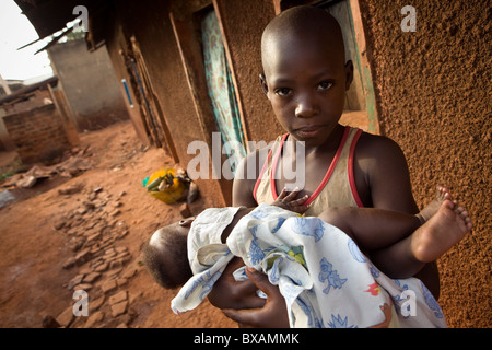 Un jeune garçon est titulaire d'un enfant dans un bidonville à Jinja, Ouganda, Afrique de l'Est. Banque D'Images