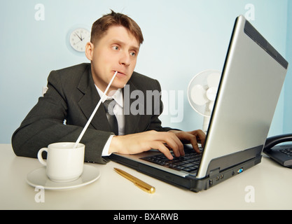 L'homme d'amusantes boit du café avec une paille sans distraire de travailler dans l'Internet Banque D'Images