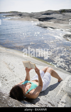 Woman Reading book on rock Banque D'Images