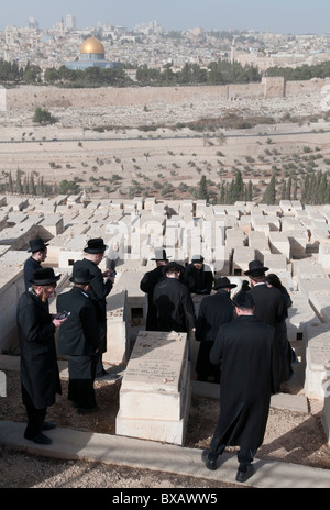 Groupe de juifs orthodoxes prier sur une tombe au cimetière du Mont des Oliviers avec la vieille ville de BKGD. Jérusalem. Israël Banque D'Images