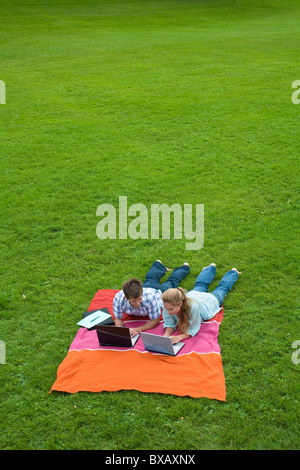 Couple lying on lawn in park et à l'aide d'ordinateurs portables Banque D'Images