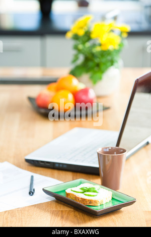 Table de cuisine avec sandwich, tasse, stylo, papier et l'ordinateur portable Banque D'Images