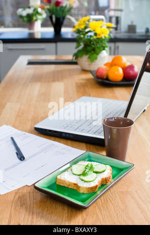 Sandwich, document papier et ordinateur portable sur une table de cuisine Banque D'Images