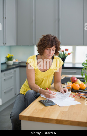 Femme assise dans la cuisine avec des factures Banque D'Images