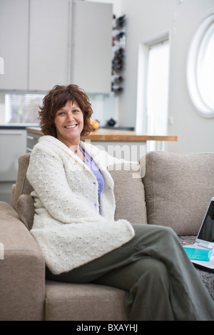 Femme assise sur un canapé, smiling Banque D'Images