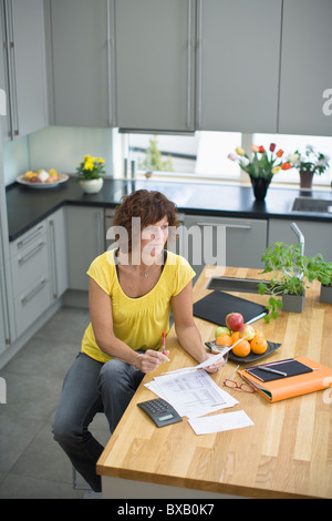 Femme assise dans la cuisine avec des factures Banque D'Images