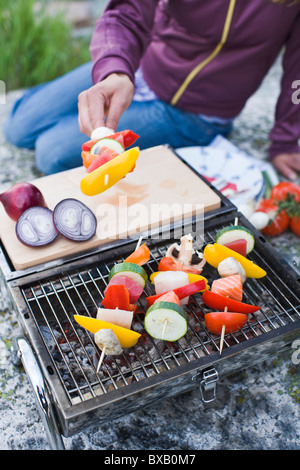 Personne tenant broche avec les légumes sur grill Banque D'Images