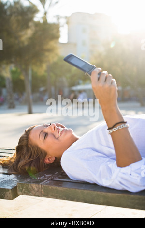 Girl lying on park bench, using cell phone Banque D'Images