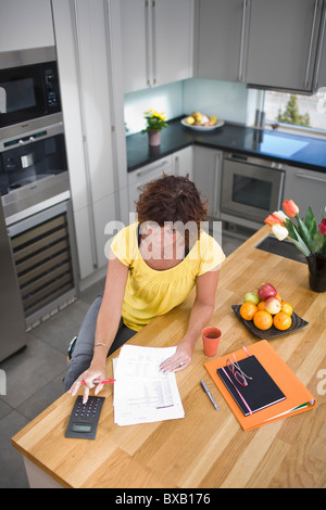 Femme assise et le calcul dans la cuisine Banque D'Images