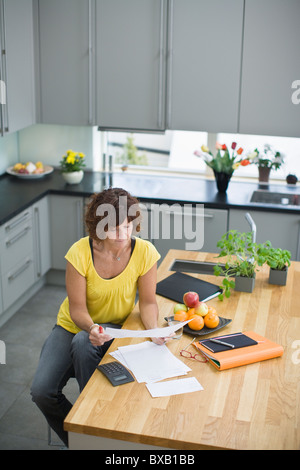 Femme assise dans la cuisine avec des factures Banque D'Images