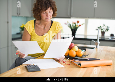 Femme assise dans la cuisine avec des factures Banque D'Images