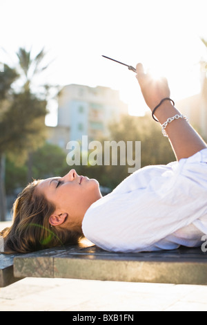 Girl lying on park bench, using cell phone Banque D'Images