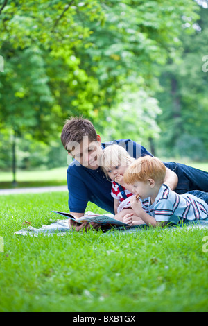 Lecture de livre père fils et fille dans park Banque D'Images