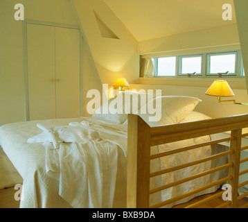 Les lampes allumées sur le mur au-dessus de lit avec oreillers et draps blancs en petite chambre mansardée Banque D'Images