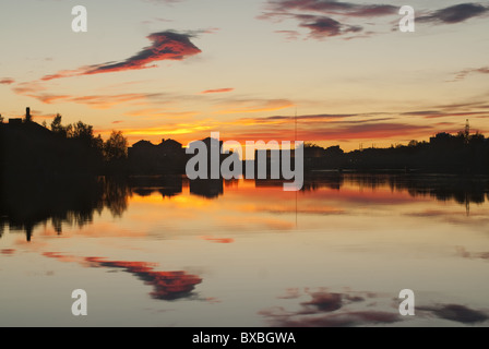 Coucher du soleil à Oulu, en Finlande. Le coucher de soleil peint le ciel rouge et jaune. Les couleurs du ciel se reflètent dans l'eau calme. Banque D'Images