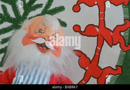 Santa est heureux et travaille dans son atelier avec les elfes. Le tissu peint à la main du Père Noël est au premier plan et porte un tablier. Les elfes dansent. Banque D'Images