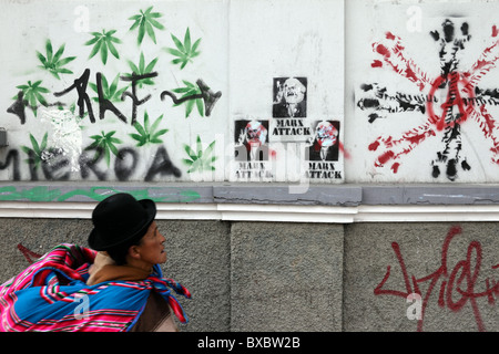 Aymara dame ou cholita passant mur avec peinture en spray des feuilles de marijuana et des graffitis de Karl Marx, la Paz, Bolivie Banque D'Images