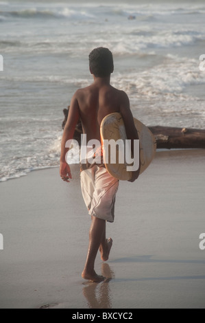 Teenage boy dans un maillot de marcher le long de la plage portant un surf Banque D'Images