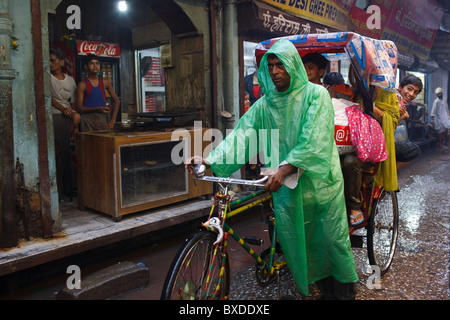 Un homme pousse un cycle riskhaw avec les enfants sous la pluie à Haridwar, Uttarakhand, Inde. Banque D'Images