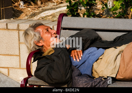 Asie sans abri man sleeping on park bench à Hong Kong, Chine Banque D'Images