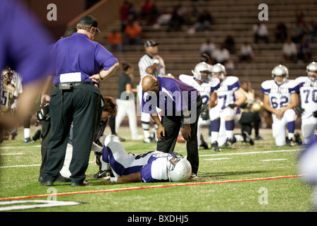 Entraîneur de football parle de joueur blessé tandis que formateur travaille sur la jambe du joueur de jeu au cours de l'école secondaire à Austin, Texas Banque D'Images